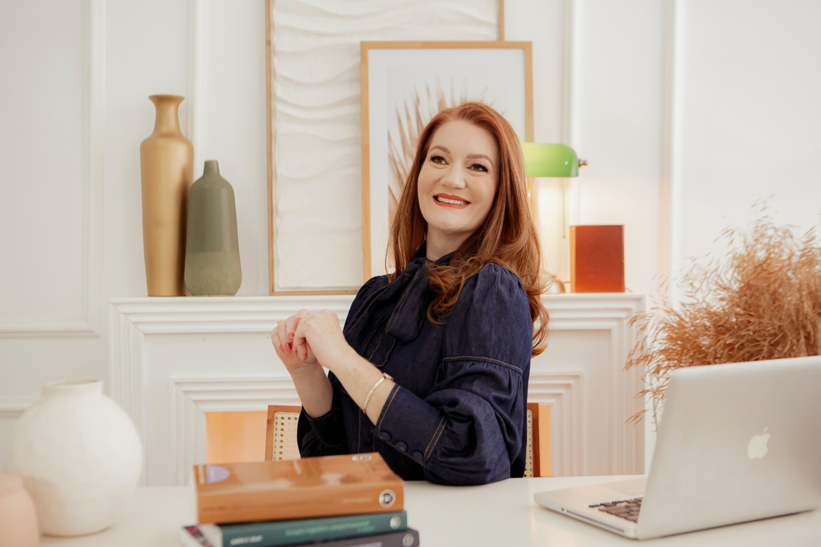 Cíntia Hoffmann em sua mesa de trabalho, ao lado de livros e notebook